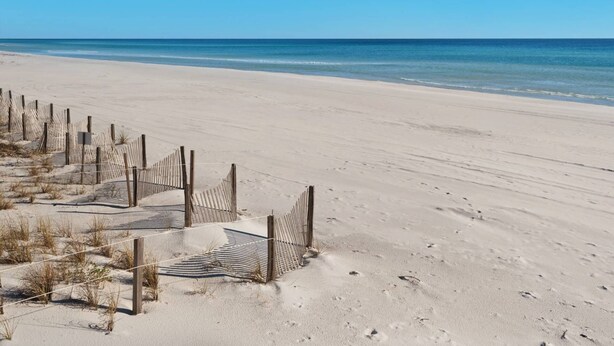 Ein sandiger Strand mit einer Holzlattenzaun und einem Schild, das zum Meer führt.