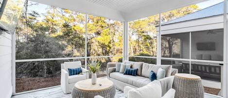 En solbeskinnet terrasse med hvidt loftsvift, sofaarrangement og fletsideborde.