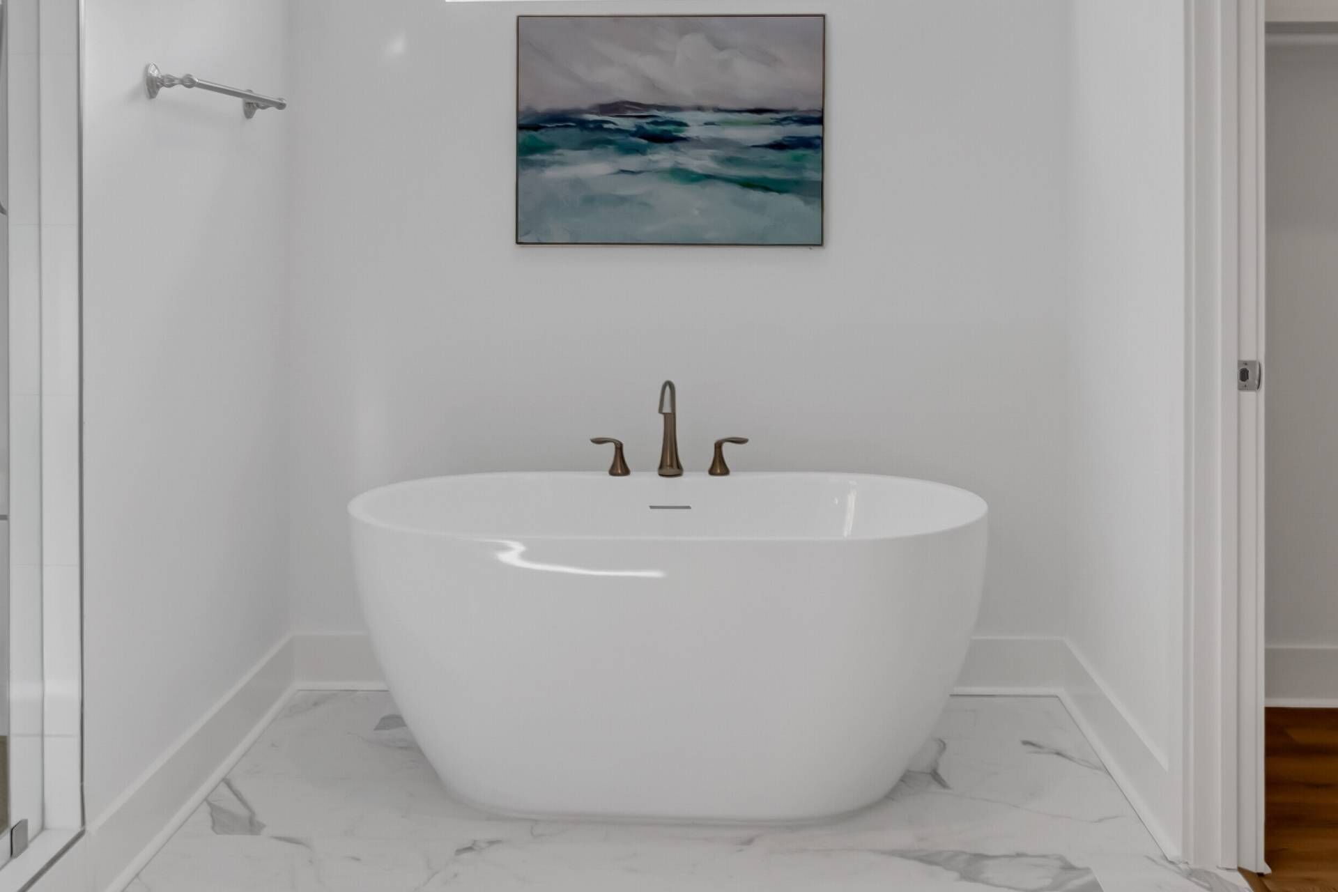 Un baño moderno con una bañera independiente, un cuadro de paisaje marino y suelo de mármol.