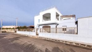 A modern white building with a gated entrance, a balcony, and a clear sky. - 3702 La Spiaggetta - Padula Fede by Barbarhouse (Porto Cesareo)