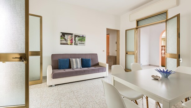 A modern living room with a sofa, a dining table with chairs, and a decorative bowl. - 3702 La Spiaggetta - Padula Fede by Barbarhouse (Porto Cesareo)