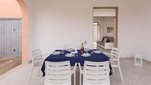 A dining area with a table set for four, white chairs, a blue tablecloth, and a bottle of champagne. - 3702 La Spiaggetta - Padula Fede by Barbarhouse (Porto Cesareo)