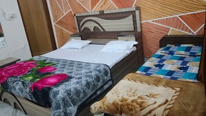 A bedroom with two beds, a wooden headboard, a patterned wall, and a framed picture. - Roomshala 153 Hotel Krishnashrya (Mathura)