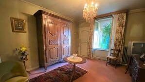 Un salón tradicional con un gran aparador de madera, una araña, un televisor y una ventana con cortinas.