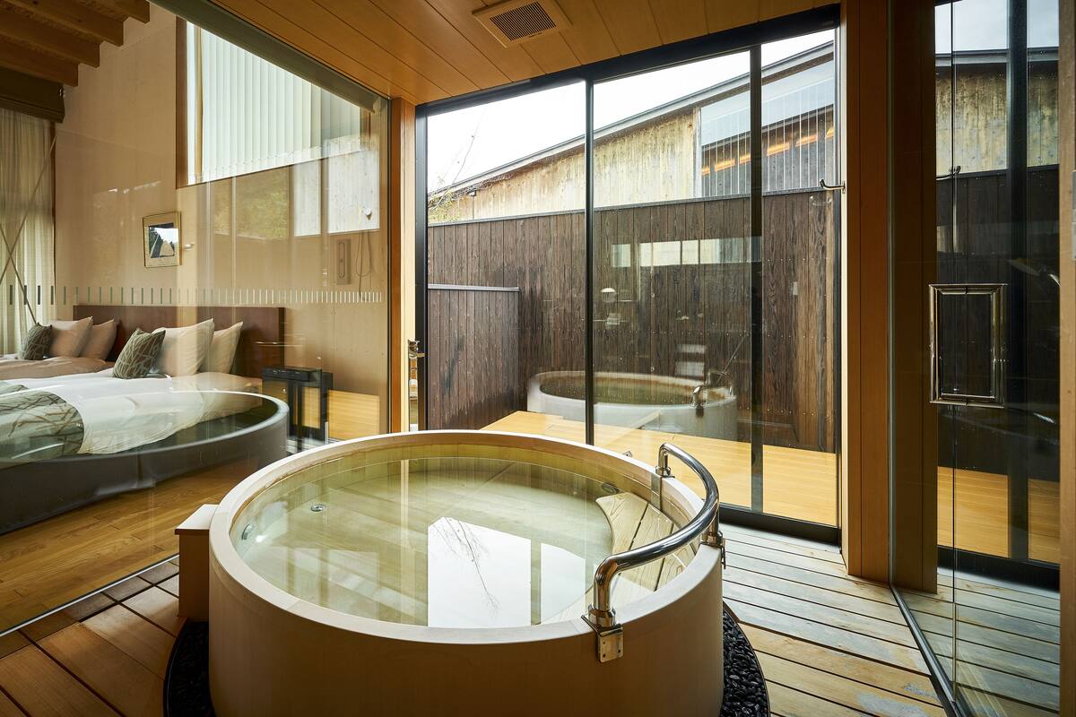 A modern bedroom with a large bed, a separate sitting area, and a glass-enclosed jacuzzi.