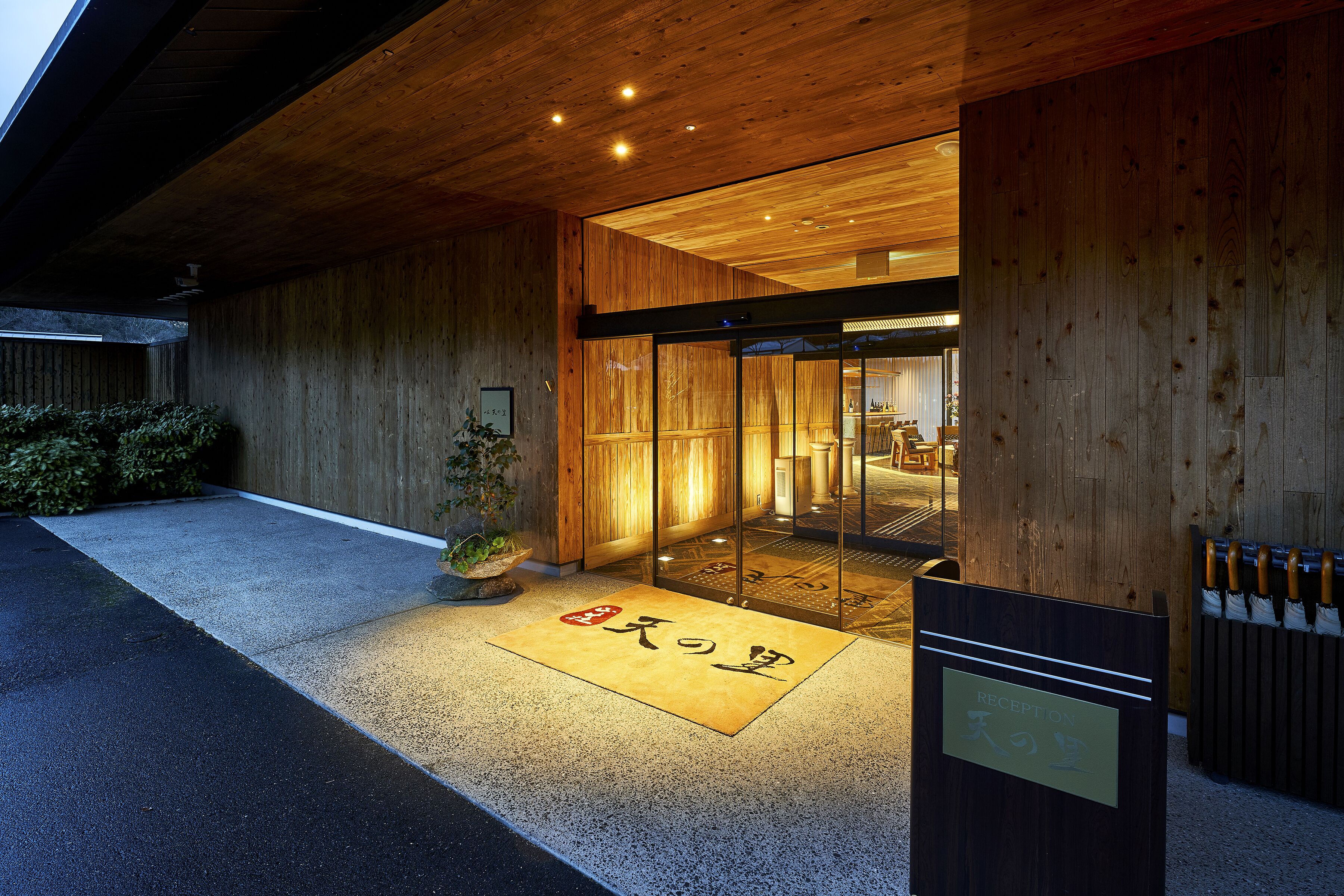 Exterior de madera con una recepción, un felpudo con caracteres japoneses y una puerta de vidrio que da al interior.