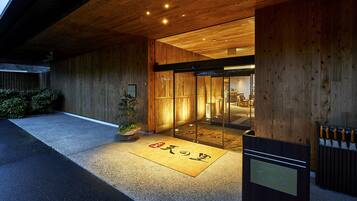 Exterior de madera con una recepción, un felpudo con caracteres japoneses y una puerta de vidrio que da al interior.