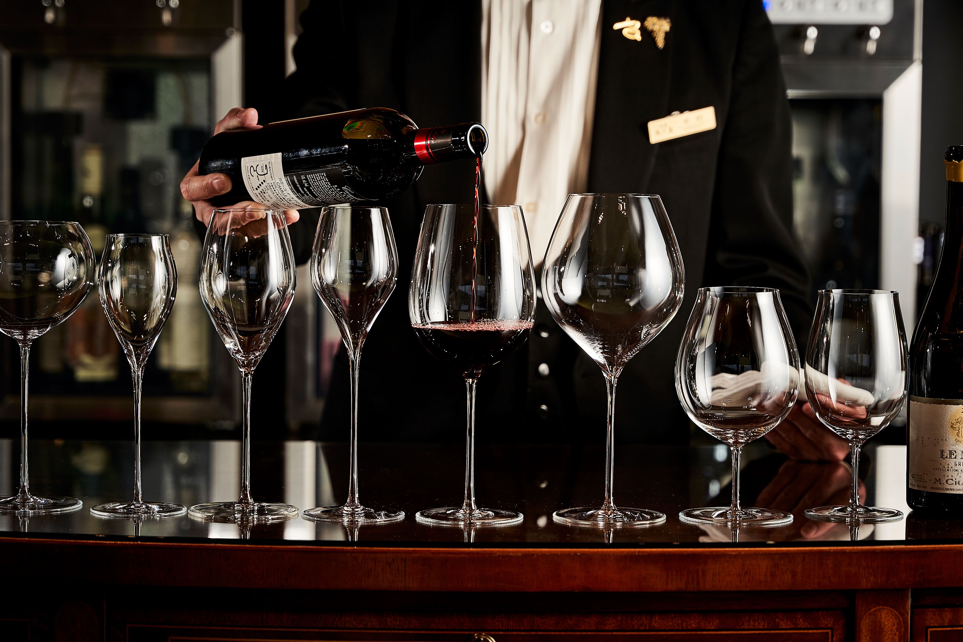 A bartender pouring wine into glasses on a bar counter.