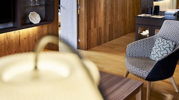 A modern interior with a wooden floor, a patterned armchair, a glass shelf with wine glasses, and a wooden cabinet.