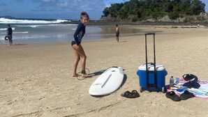 A sandy beach with a surfboard, a cooler, and beach gear.