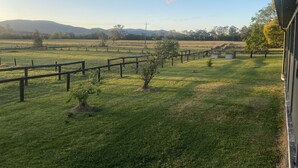 A view of a grassy field with a wooden fence, trees, and distant mountains.
