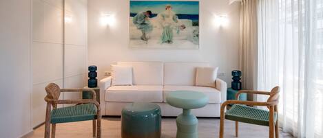A modern living room with a white sofa, two green chairs, and a round ottoman.