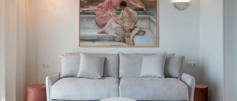 A modern living room with a grey sofa, two round tables, and a large painting of a ballerina on the wall.