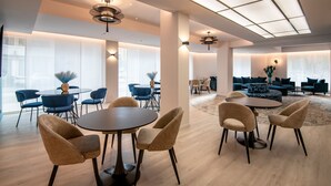 A modern interior with round tables and chairs, large windows, and a high ceiling with skylights. - Résidence Hôtelière Chambord (Menton)