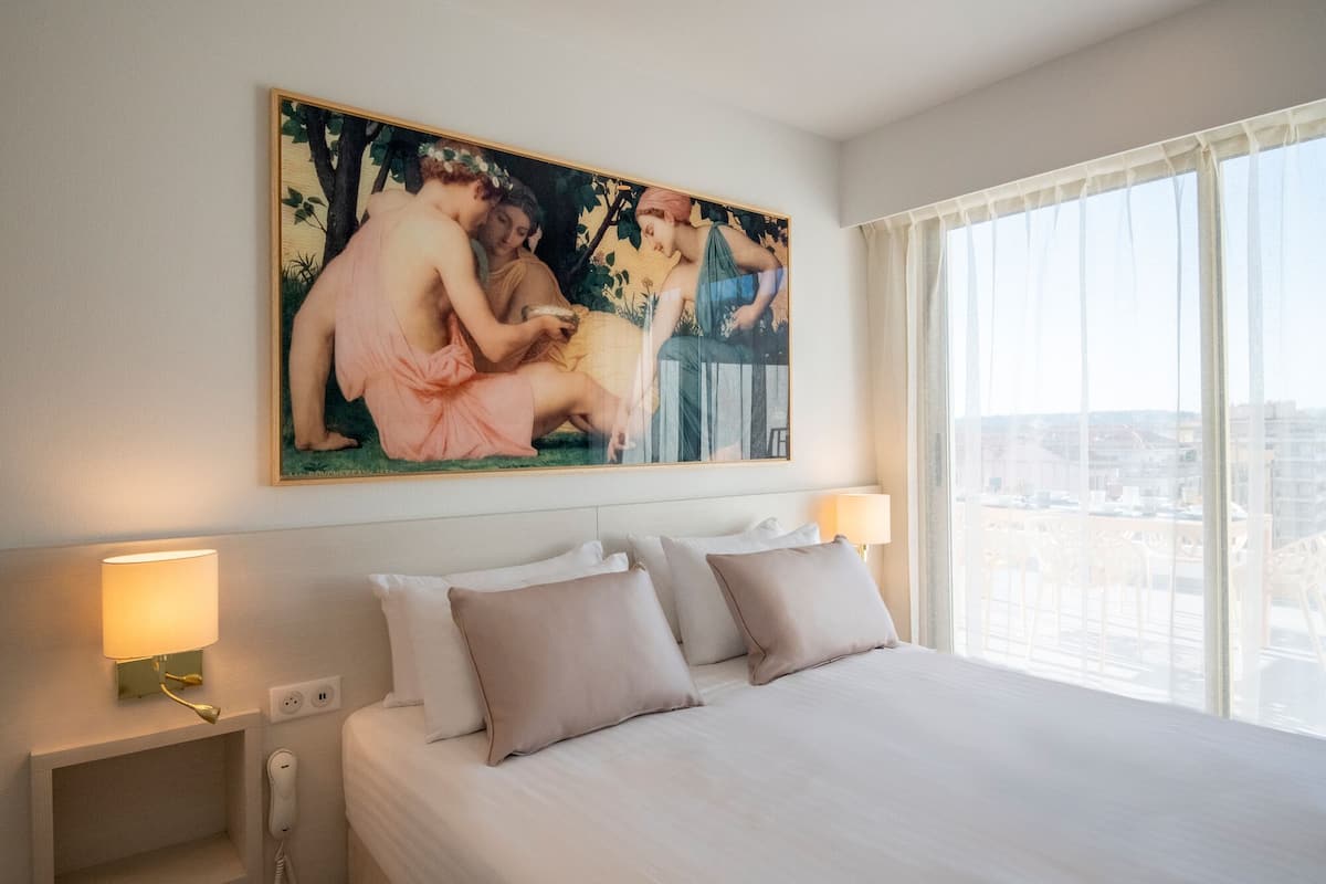 Ett hotellrum med en stor säng, två sänglampor, en tavla på väggen och utsikt över staden genom fönstret.