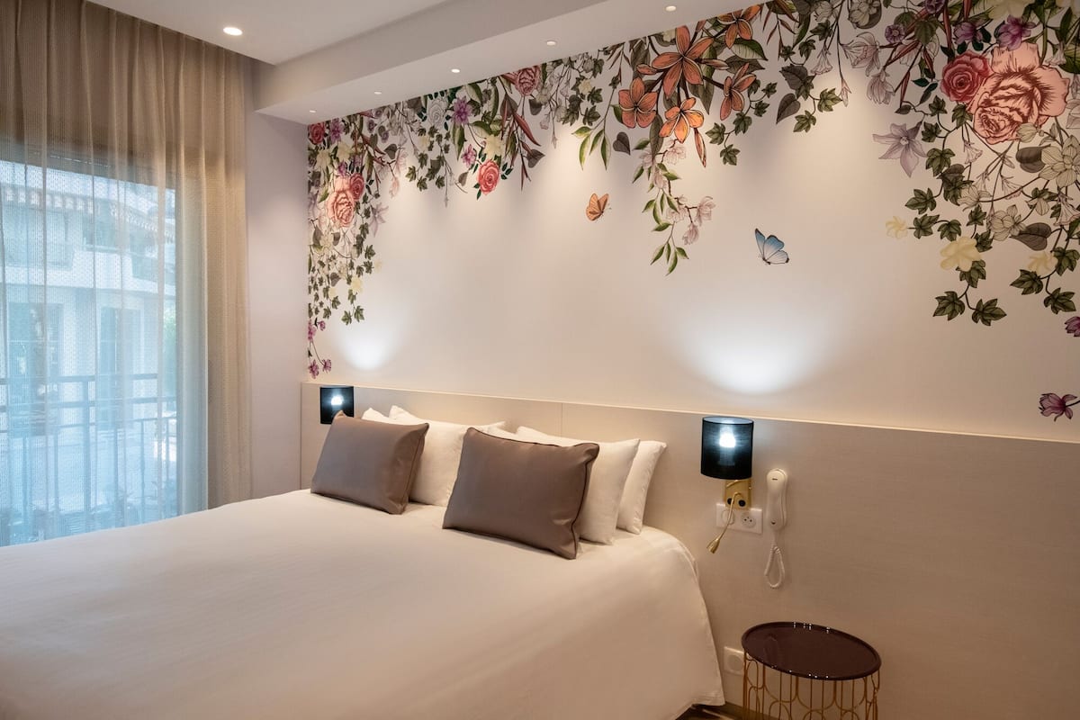 Ett hotellrum med en stor säng, en dekorativ vägg med ett blommönster, ett litet runt bord och en telefon på väggen.