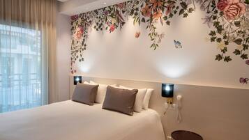 Habitación de hotel con una cama grande, un diseño floral decorativo en la pared, una mesita redonda pequeña y un teléfono en la pared.