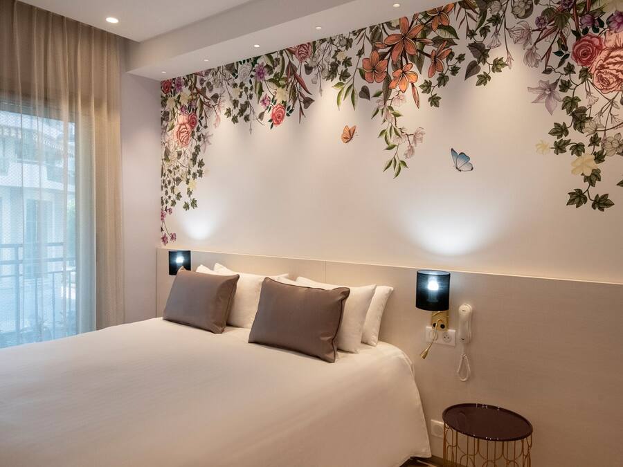 Habitación de hotel con una cama grande, un diseño floral decorativo en la pared, una mesita redonda pequeña y un teléfono en la pared.