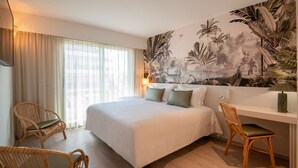 A hotel room with a large bed, two wicker chairs, a desk, and a tropical mural on the wall. - Résidence Hôtelière Chambord (Menton)