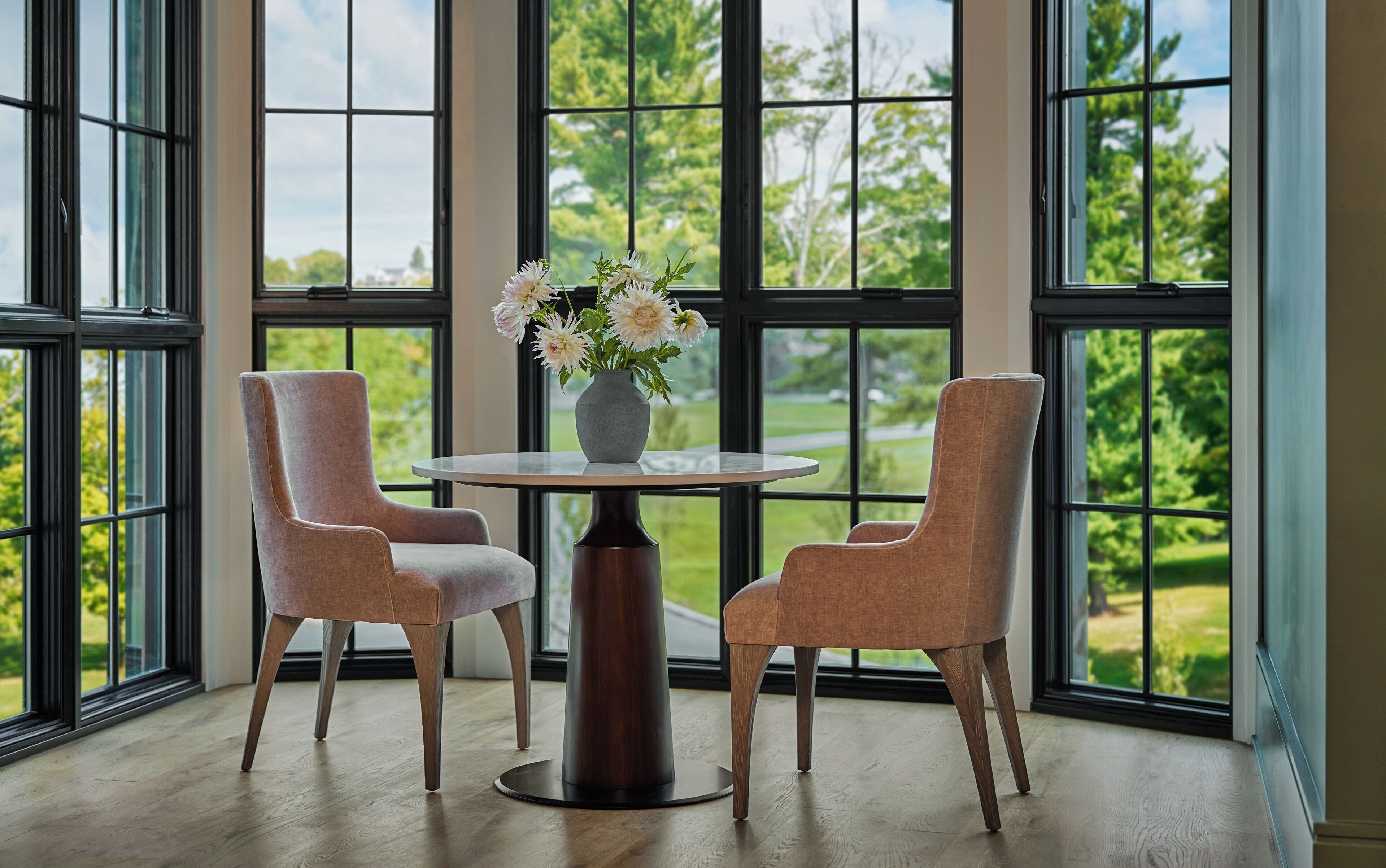 Una habitación con una mesa redonda, dos sillas y un florero con flores.