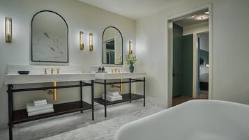 A modern bathroom with two sinks, a large mirror, and a bathtub.