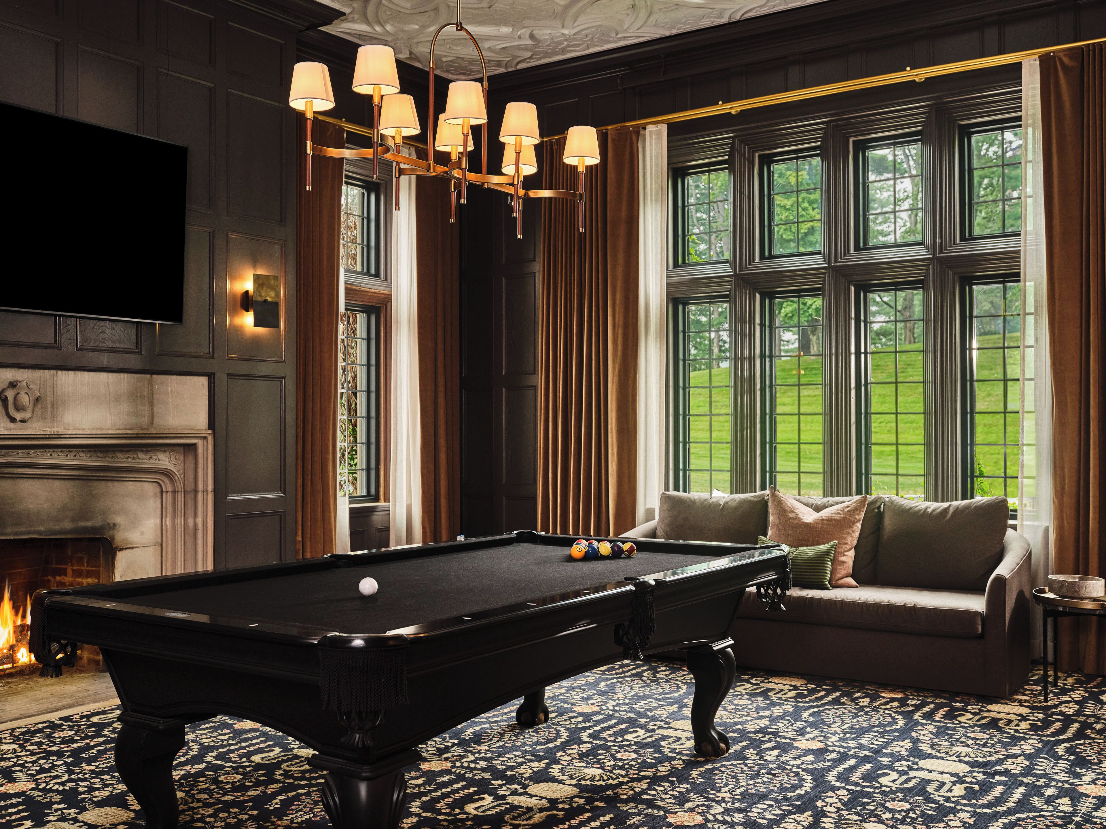 A pool table with a chandelier, a sofa, and a fireplace.