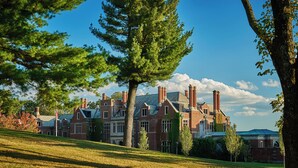 A large brick building with multiple chimneys, surrounded by trees and a grassy hill. - Pendry Natirar (Far Hills)