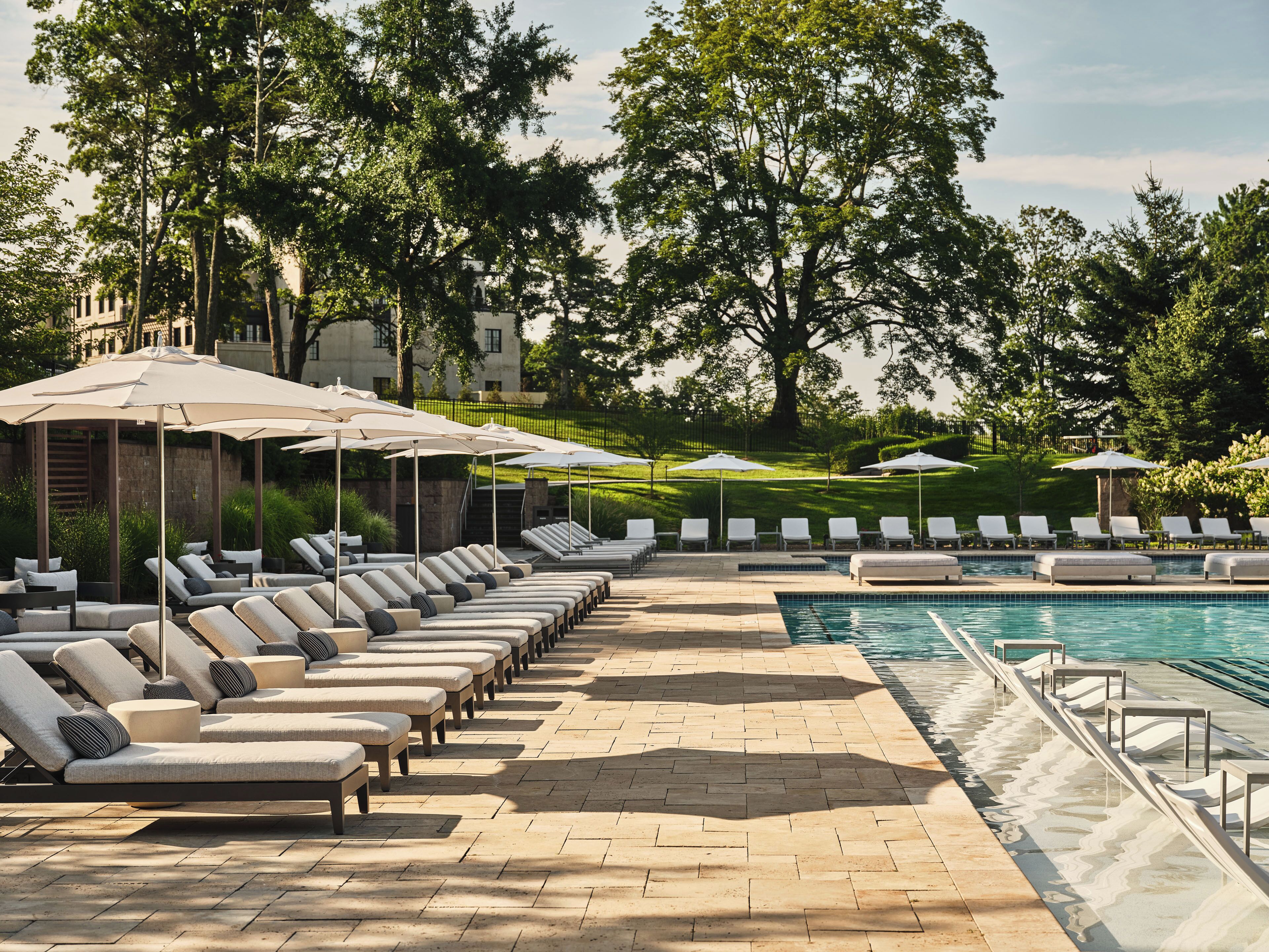 A poolside area with lounge chairs and umbrellas, surrounded by trees and a building in the background.