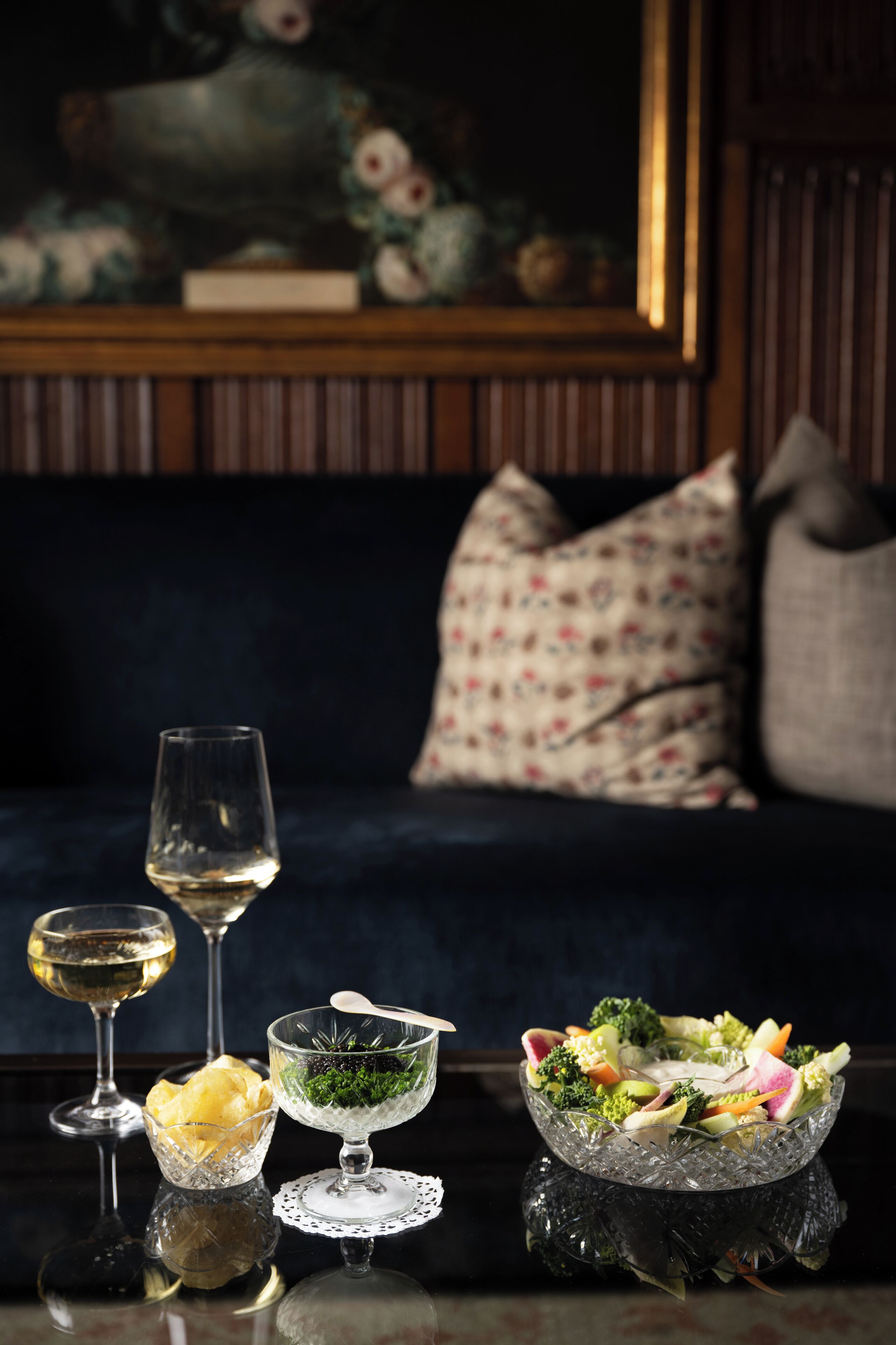 A dining table with a bowl of salad, two wine glasses, and a glass bowl with a spoon.