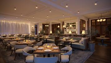 A spacious, elegantly furnished dining area with multiple seating options, including tables and sofas, and a bar area with a brick wall and shelves of bottles.