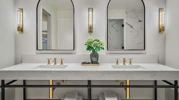 A bathroom with a white marble sink and vanity, two gold faucets, a vase with green plants, and two wall-mounted mirrors with black frames.