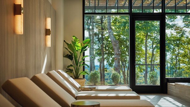 A modern interior with a row of beige sofas and a large window offering a view of trees. - Pendry Natirar (Far Hills)