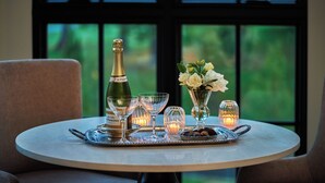 A table set with a bottle of champagne, glasses, a vase with flowers, and a candle. - Pendry Natirar (Far Hills)