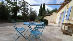 A patio with a table and blue chairs, surrounded by a garden and a building with blue shutters. - Maison Aix en Provence (Aix-en-Provence)