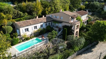 Una amplia casa con piscina, rodeada de árboles y un muro de piedra.