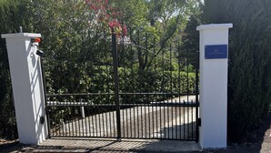 A gated entrance with a metal gate, a white wall, and a sign reading 'Les Petites Terrasses.' - Les Petites Terrasses (Grasse)