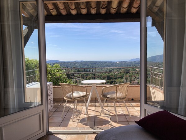 A balcony with a table and chairs, offering a view of a landscape with trees and distant hills.
