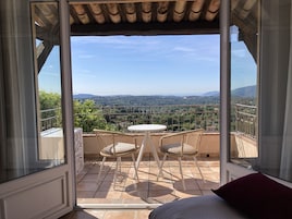 Un balcón con mesa y sillas, con vistas a un paisaje de árboles y colinas distantes.