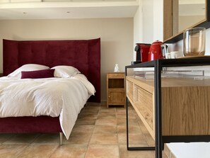 A modern bedroom with a large bed, a wooden nightstand, a red coffee maker, and a mirror above the dresser. - Les Petites Terrasses (Grasse)