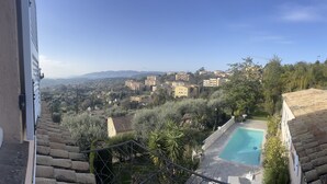 A view from a balcony overlooking a swimming pool, with a cityscape in the background. - Les Petites Terrasses (Grasse)