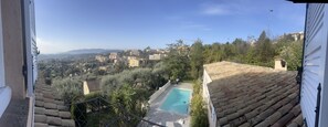 A view from a balcony overlooking a swimming pool, with a cityscape in the background. - Les Petites Terrasses (Grasse)