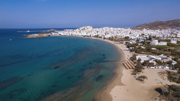 An aerial view of a coastal town with a beach, clear blue waters, and white buildings. - Flisvos Beach Apartments (Naxos)