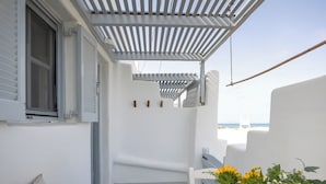A white balcony with a wooden pergola, a wicker plant pot, and a view of the sea. - Flisvos Beach Apartments (Naxos)