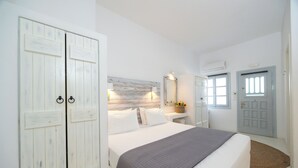A bedroom with a large bed, a wardrobe, a nightstand, and a door with a window. - Flisvos Beach Apartments (Naxos)