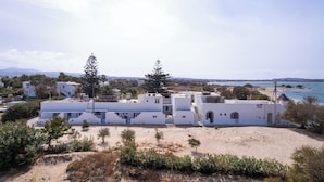 A coastal building with a white facade, a sandy foreground, and a view of the sea and distant mountains. - Flisvos Beach Apartments (Naxos)