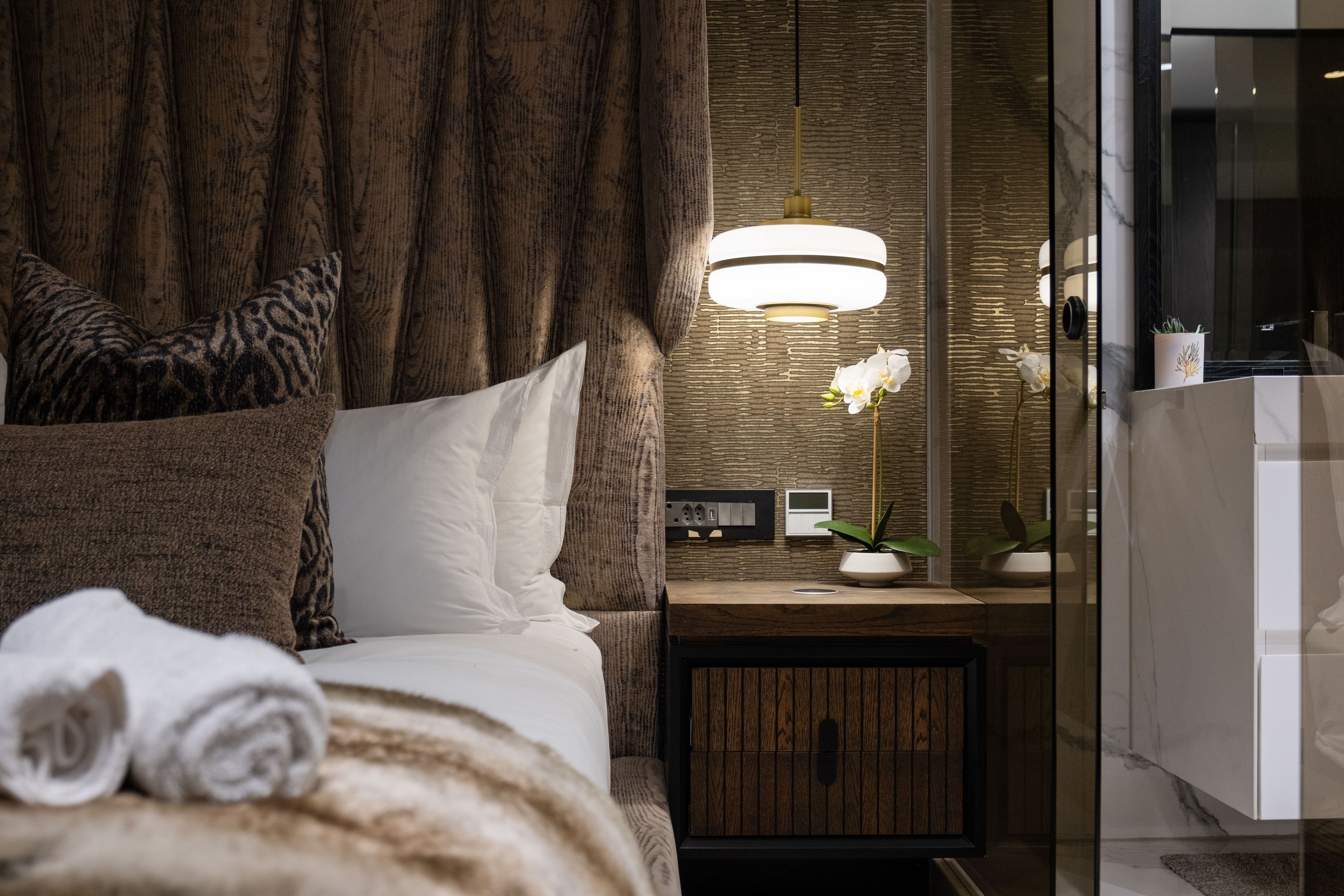 Une chambre à coucher moderne avec une tête de lit en bois, une table de chevet avec une lampe, un miroir et une petite plante en pot.