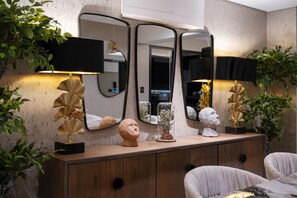 Una sala de estar moderna con un mueble de madera, tres espejos y objetos decorativos, incluyendo una lámpara dorada y esculturas.