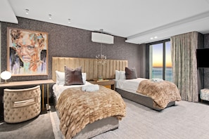 A modern hotel room with two beds, a large painting on the wall, a view of the ocean, and a flat-screen TV. - Aurum 501 (Cape Town)