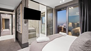 A modern hotel room with a large bed, a flat-screen TV, a glass-enclosed shower area, and a city view. - Aurum 501 (Cape Town)