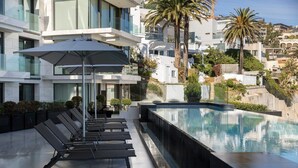 A modern hotel pool area with sun loungers and a large umbrella, surrounded by lush greenery and palm trees. - Aurum 501 (Cape Town)
